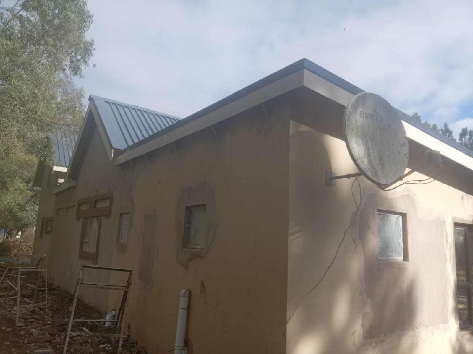 House exterior with fresh plaster patches and new metal roof sheeting under a cloudy sky
