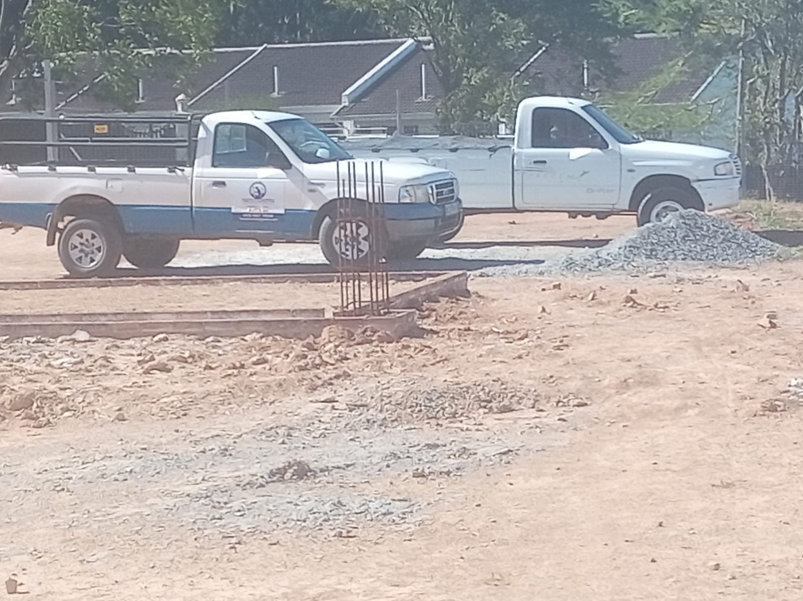 Reinforced foundation trenches with steel rebar at a new build site, work bakkies parked nearby